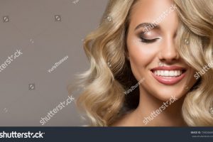 stock-photo-blonde-woman-with-curly-beautiful-hair-smiling-on-gray-background-730048489