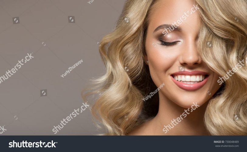 stock-photo-blonde-woman-with-curly-beautiful-hair-smiling-on-gray-background-730048489