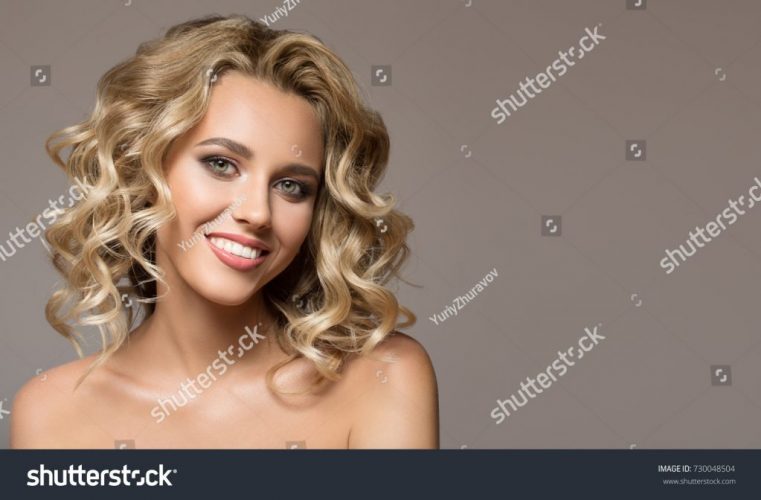 stock-photo-blonde-woman-with-curly-beautiful-hair-smiling-on-gray-background-730048504