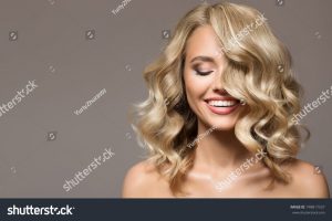 stock-photo-blonde-woman-with-curly-beautiful-hair-smiling-on-gray-background-748817557